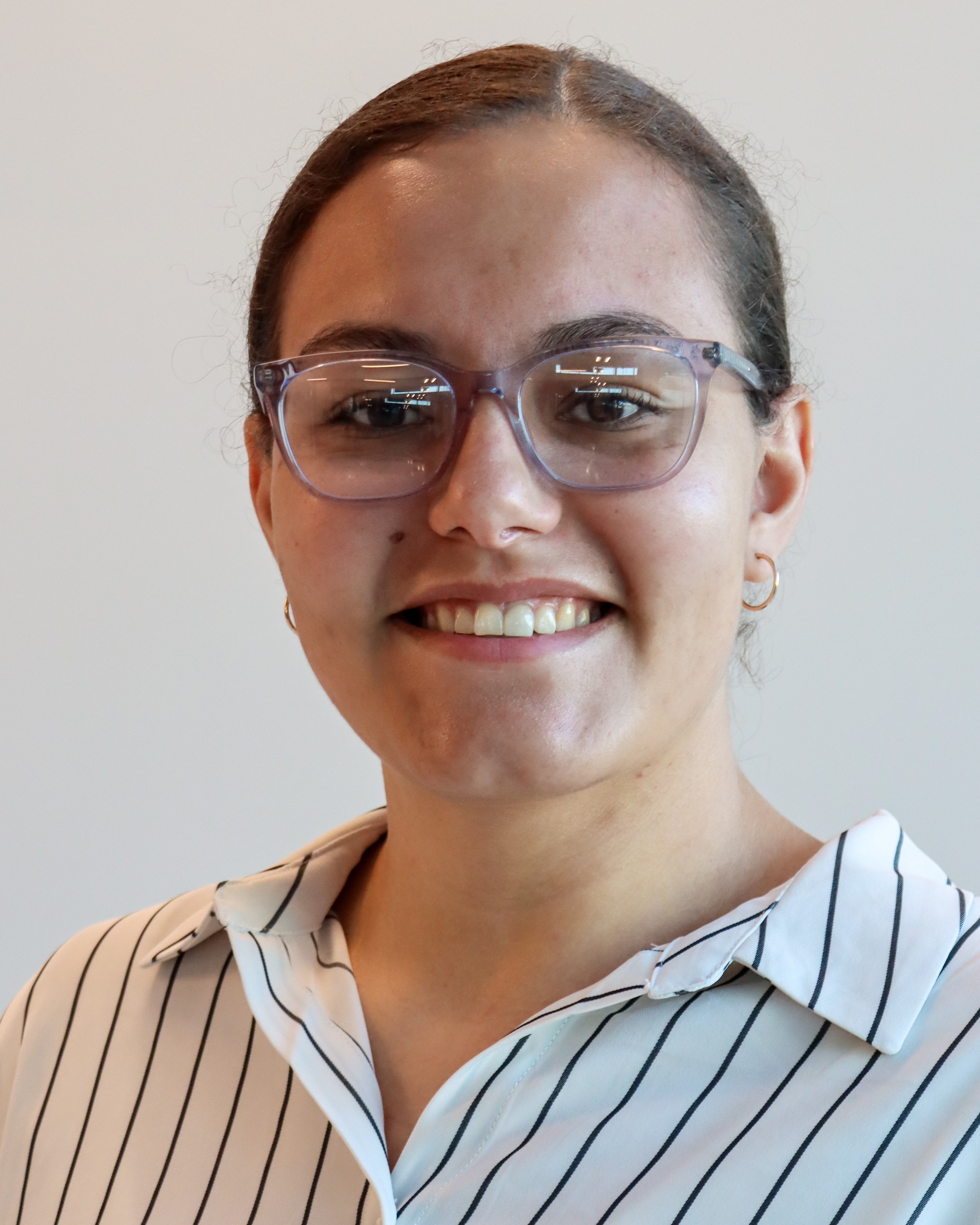 Professional headshot of a woman in a white and 
            navy striped blouse and see-through purple glasses smiling directly into the camera.